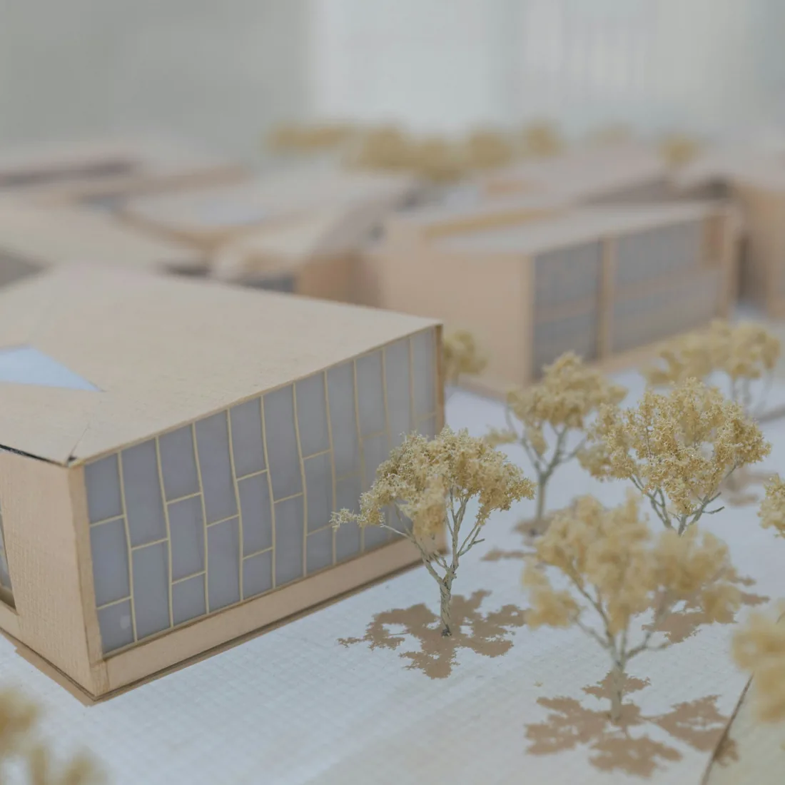 Maqueta blanca de un conjunto de edificios sobre una superficie clara, con volúmenes recortados y cubiertas inclinadas
